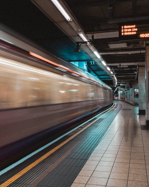 Image of a moving train at an underground station with tiled flooring, metal railings, and overhead digital departure boards displaying destinations such as Richmond, Circle Line, and Wimbledon. The platform is clean with non-slip yellow safety lines along the edge and well-lit surroundings. The station's walls are tiled, and the lighting fixtures cast a bright, even glow. The scene emphasizes cleanliness and maintenance typical of an urban rail environment, highlighting the importance of surface cleaning and sanitisation by professional cleaning companies like Cleaner Harringay, especially near busy transportation hubs such as Harringay Green Lanes station.