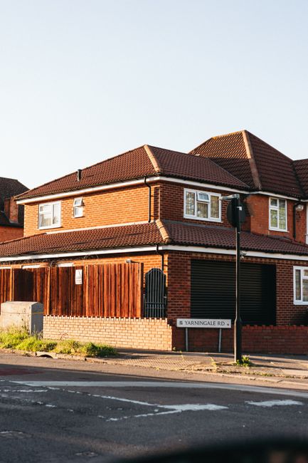 A two-story brick residential building with a red-tiled roof situated on Yarningale Road. The exterior features white-framed windows, some with small safety bars, and a black garage door. A wooden fen